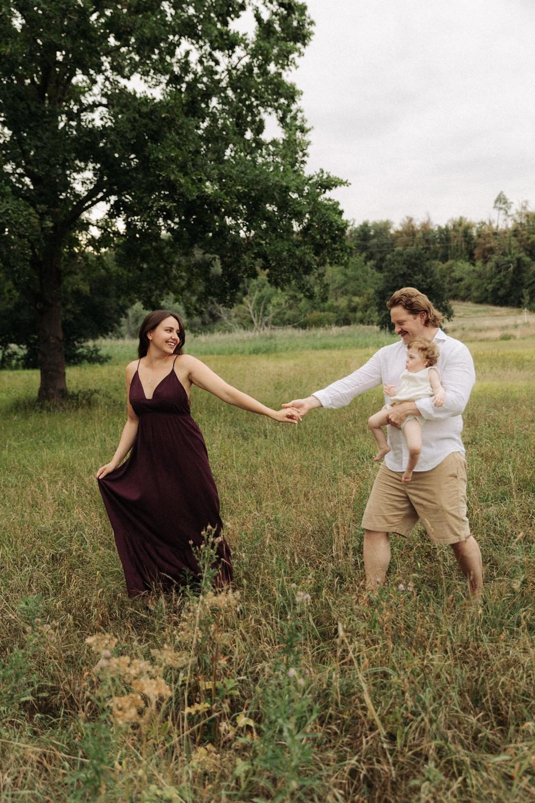 Julia und Sven laufen Hand in Hand mit ihrem Kind über eine Sommerwiese